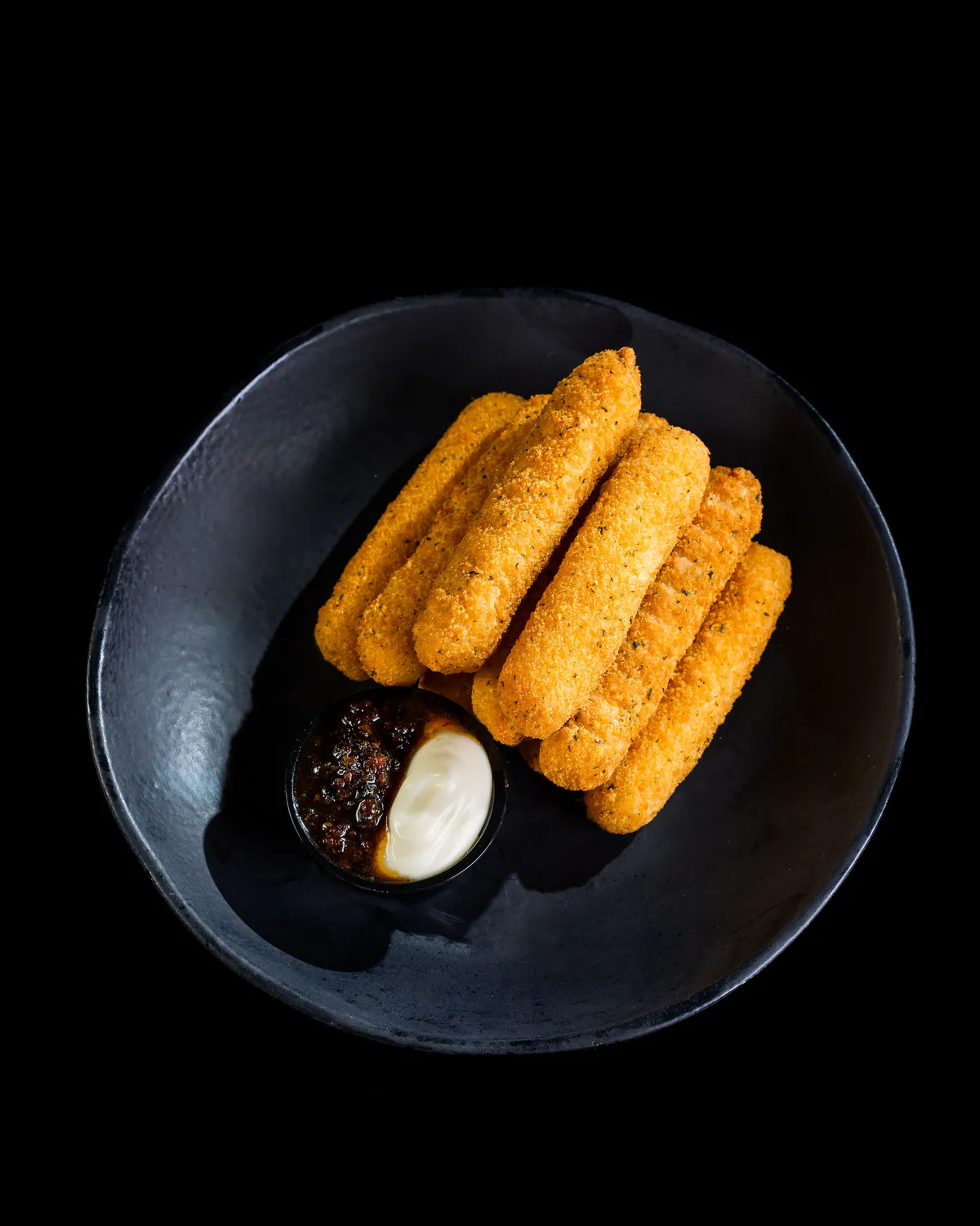 Prato preto com palitos empanados e dois molhos