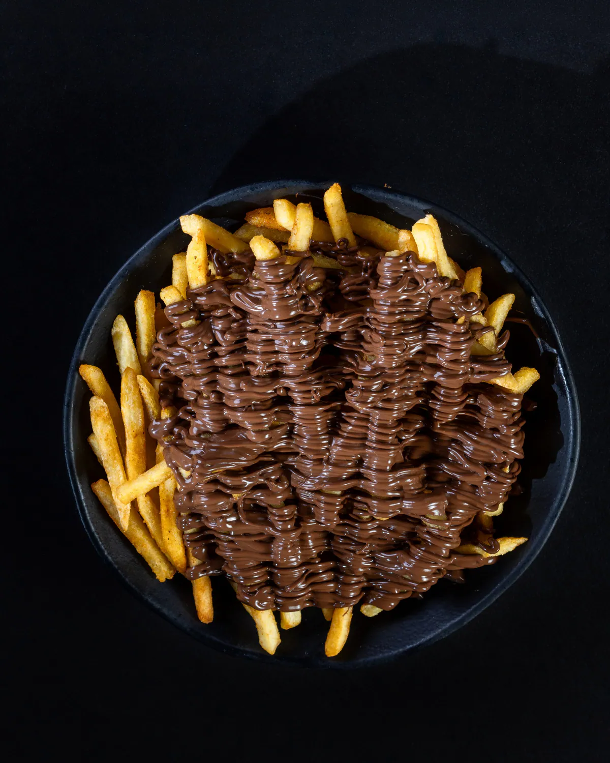 Prato preto com batata frita coberta por calda escura